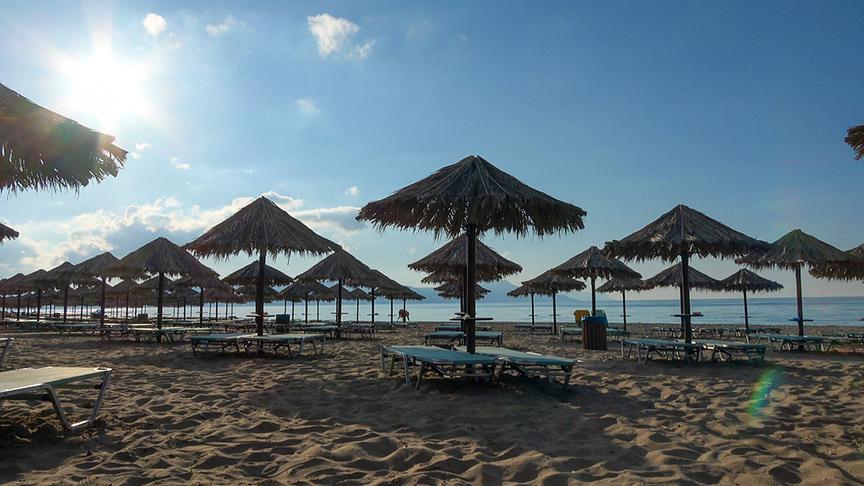Strand in strahlendem Sonnenschein mit Strandliegen und vielen Sonnenschirmen aus Naturmaterial