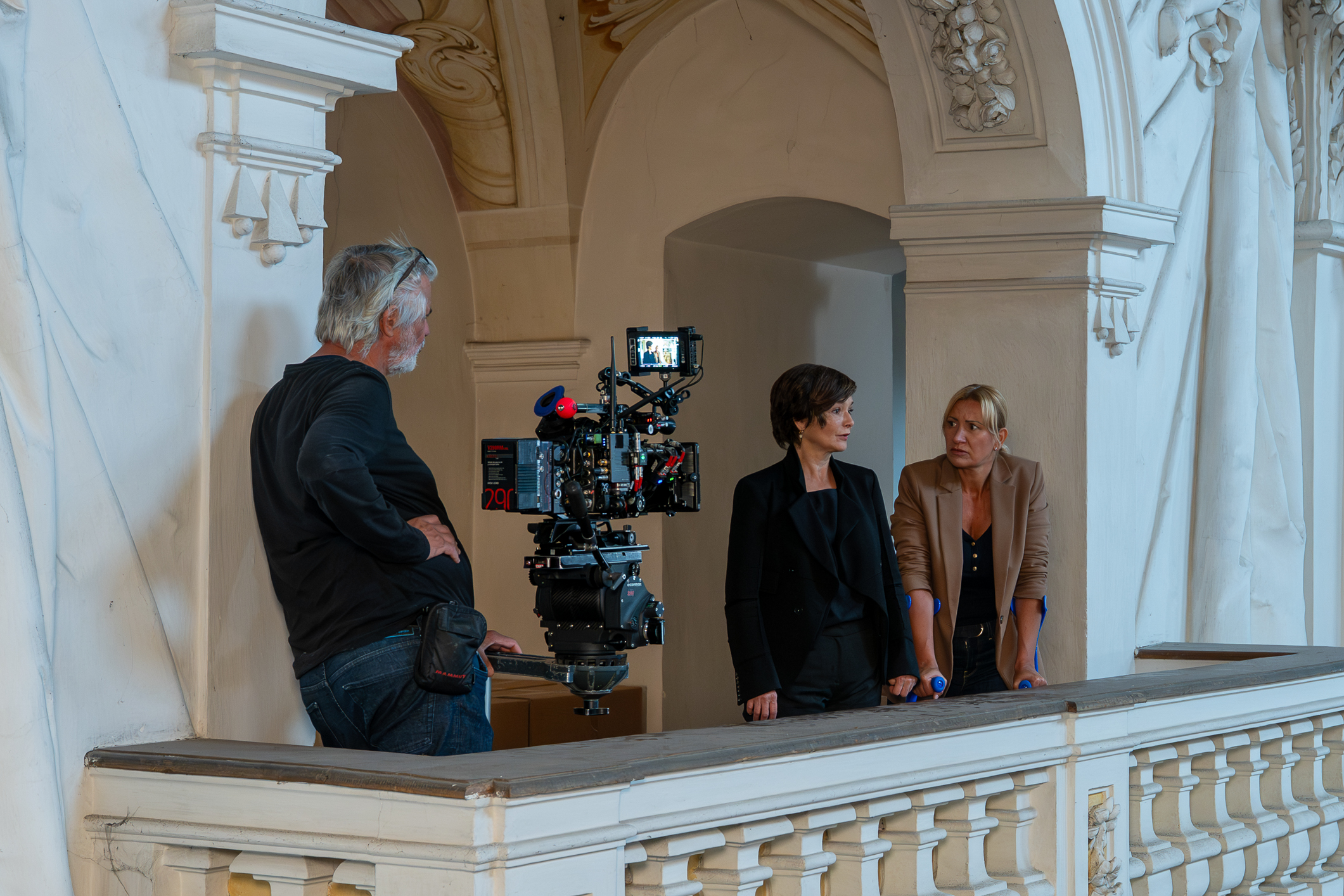 Ein Kameramann filmt Katharina Stemberger und Angelika Niedetzky, die in einer prunkvollen Galerie miteinander sprechen.