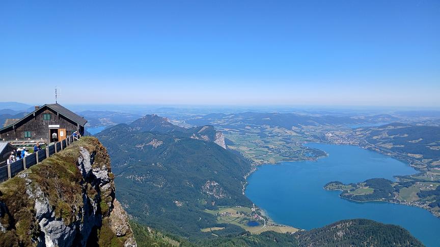 Aufnahme von einem Berg mit exponierter Hütte hinunter auf eine weite Seenlandschaft.