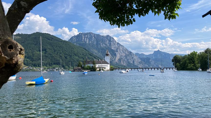 Ein See umgeben von hohen Bergen. Auf einer Insel im See Schloss Ort.