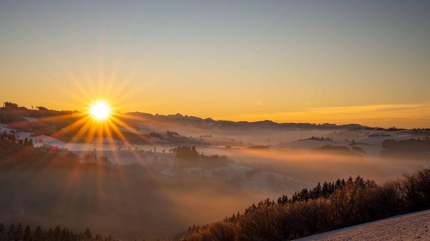 © Harald Haselsteiner Sonnenaufgang über einem teils bewaldeten, verschneiten und nebeligen Tal