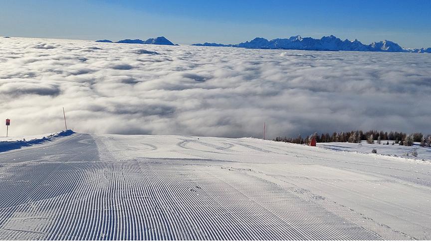 Die präparierte Skipiste scheint direkt in ein Wolkenmeer zu enden, während darüber der blaue Himmel strahlt.