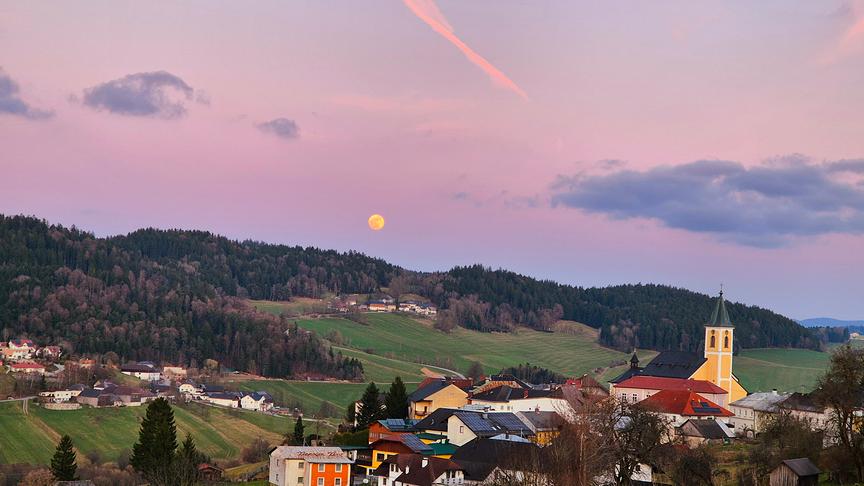 Abendrot mit Mond über einem Hügel und einem Dorf