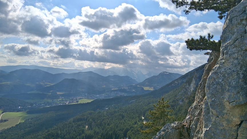 Blick über hügeliges Tal mit blauem, hellem Himmel und bauschigen Wolken
