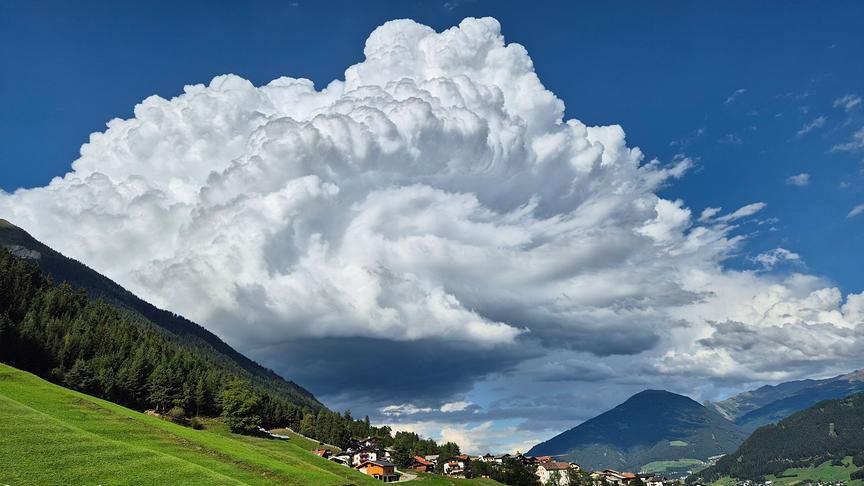 Hohe, bauschige Wolke über einem Tal am blauen Himmel.