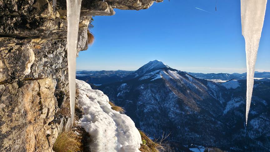 © Christian Hahn Von einem Felsen hängen Eiszapfen vor einem schneebedeckten Bergepanorama