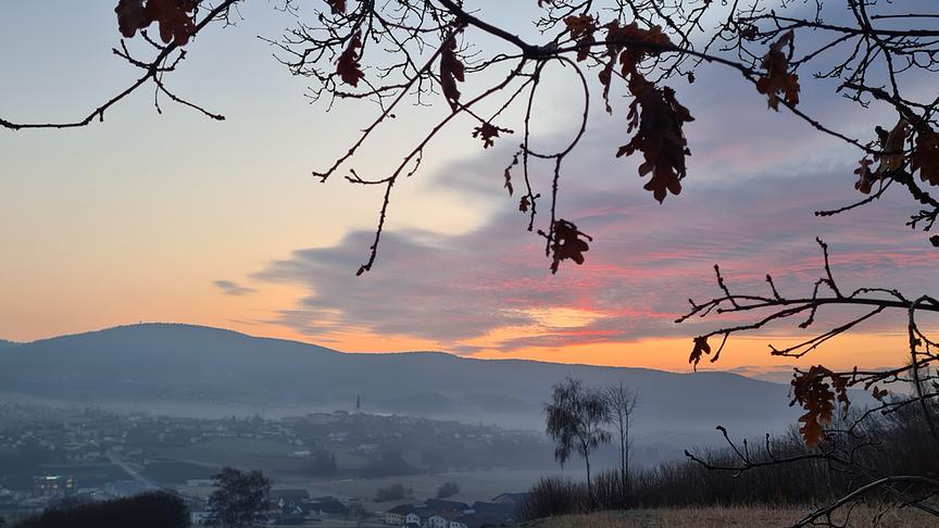 Rot-orange Morgendämmerung mit Wolken über einem noch etwas vernebelten Tal