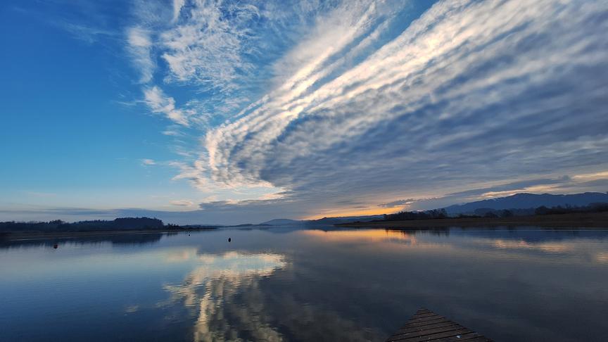 Ruhiger See, darüber eine interessante langgezogene Wolkendecke, die die Hälfte des Himmels bedeckt und sich im See spiegelt 