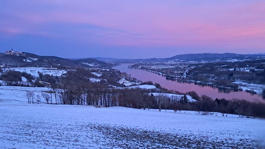 Blick auf rot-bläulichen Himmel, der Farbe in den Fluss und die verschneite Hügellandschaft bringt.
