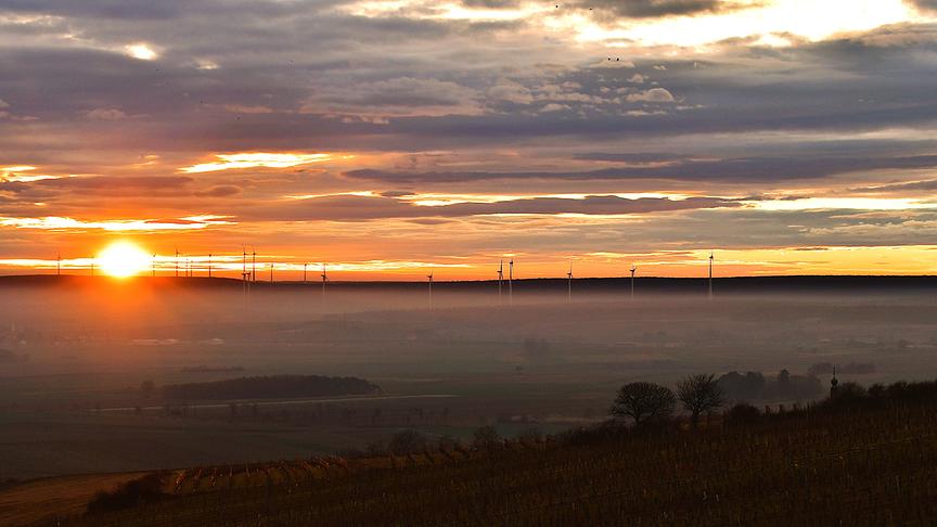 Der Nebel zieht über die flache mit Windrädern versehene Ebene bei warmer Dämmerungsstimmung.