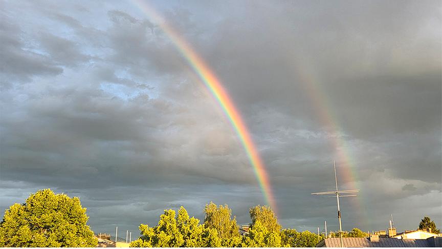 Graue Wolken vor denen ein doppelter Regenbogen den Boden trifft.