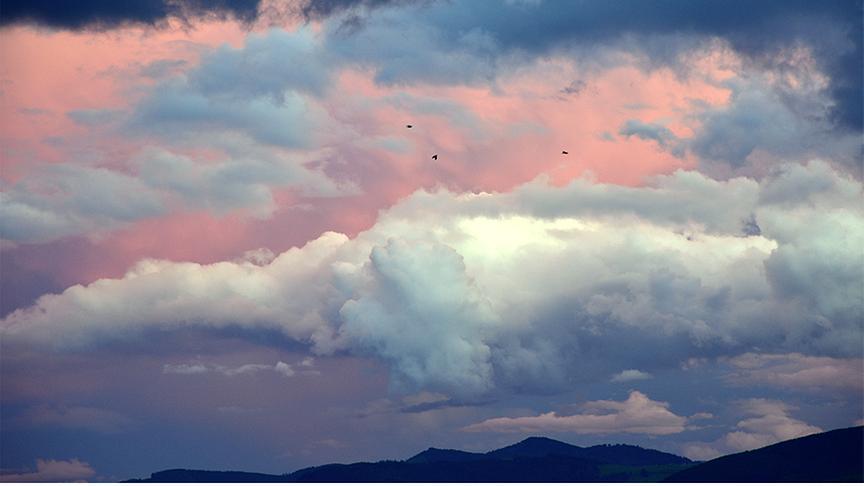 Rosa-dunkle Stimmung mit Wolkenformationen und drei Vögeln am Himmel fliegend über den Silhouetten von Bergen.