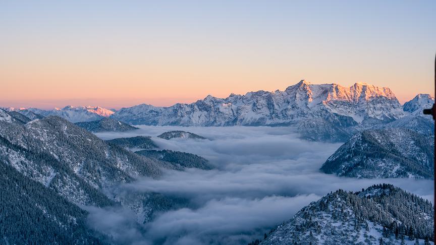 © Alois Redolfi Eine Wolkendecke hängt zwischen den Bergen, die Sonne färbt den Himmel ein