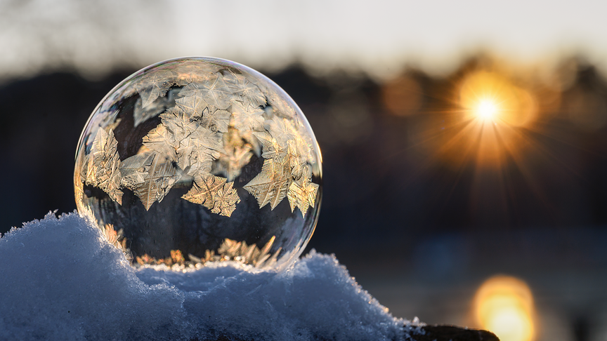 Gefrorene Seifenblase mit Eiskristallmuster, die von der Sonne angestrahlt wird.