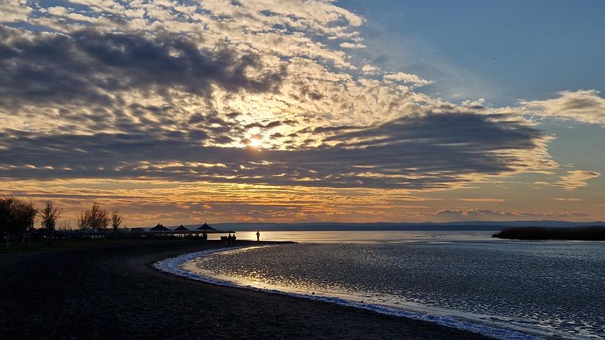 Wolkiger Sonnenuntergang über vereistem See und Uferstrand