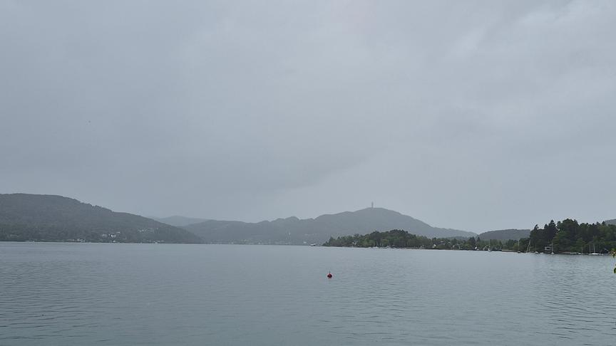 Graue, neblige Schlechtwetter-Stimmung über einem See mit Bergen im Hintergrund