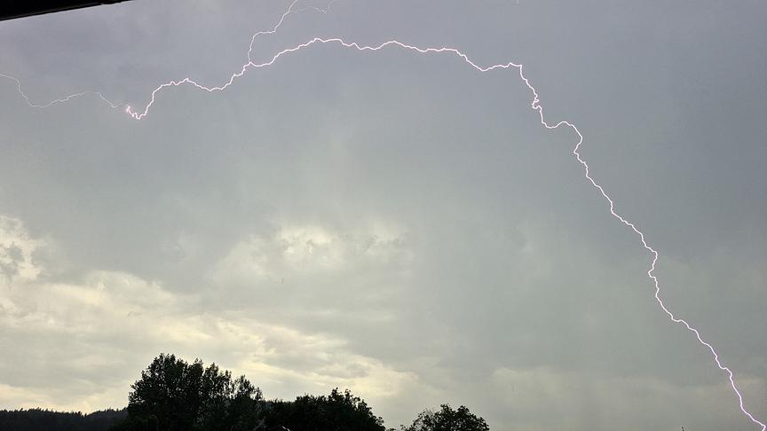 Ein Blitz zieht sich vom wolkenverhangenen, grauen Himmel Richtung Boden.