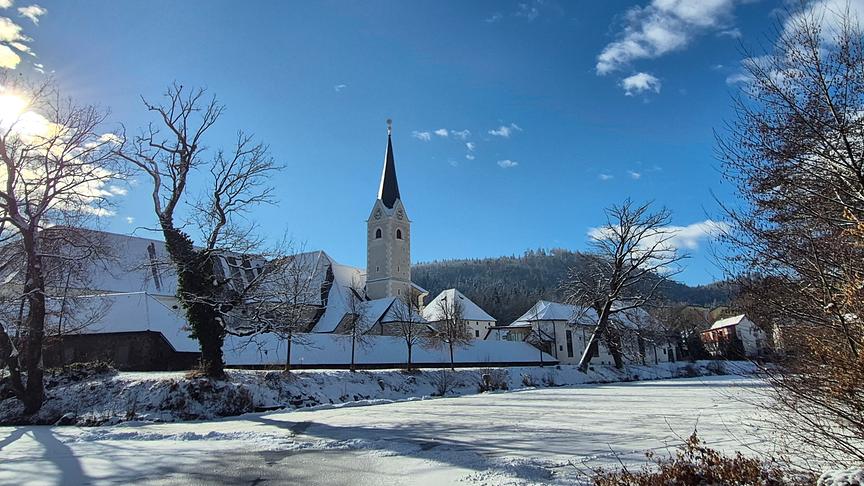 Verschneite Wiese, Häuser und Kirche im Sonnenschein