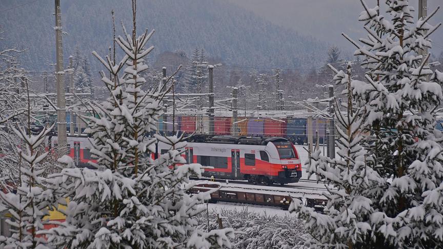 Zwischen schneebedeckten Tannen leutet ein rot-weißer Zug hindurch