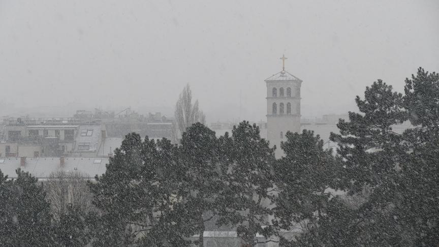 Starker Schneefall trübt die Sicht über Bäume, Dächer und Kirche