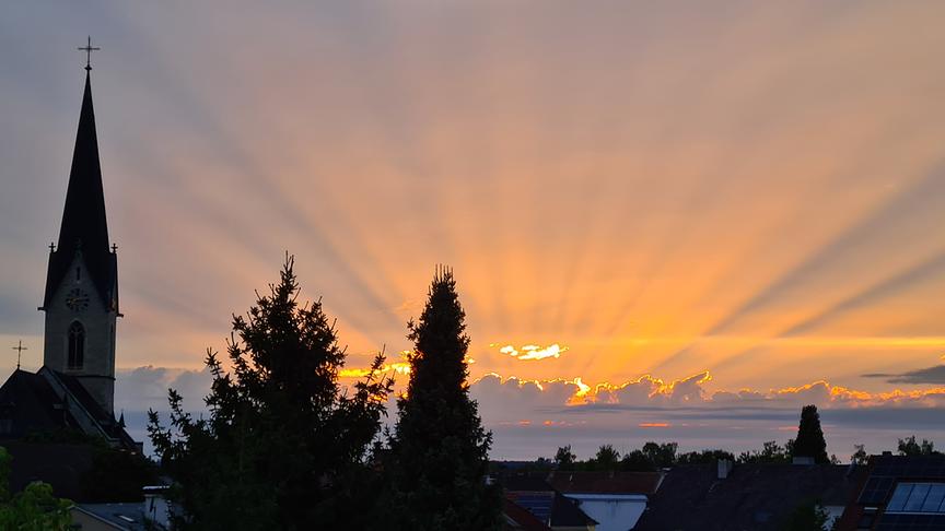 Sichtbare, warme Sonnenstrahlen einen Sonnenuntergrangs strahlen über Wolken hinweg.