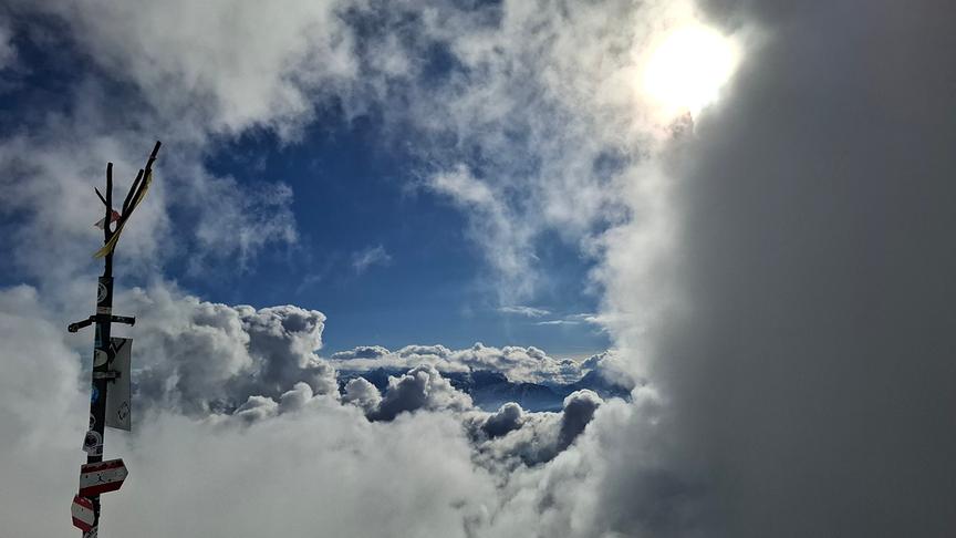 Die Wolken scheinen überall zu sein und bedecken vor allem die rechte und untere Seite im Bild, ein Wolkenfenster gibt Ausblick auf die beeindruckenden Wolkenformationen im Hintergrund und den blauen Himmel darüber.