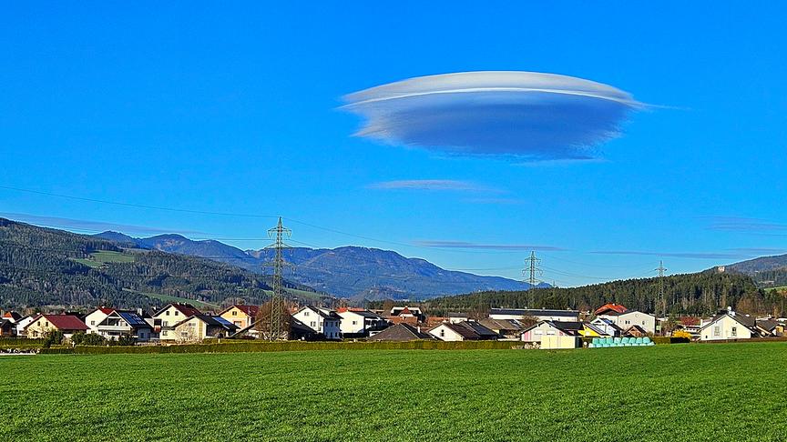 Interessant geformte Wolke am blauen Himmel über bewaldeten Bergen und einer Siedlung