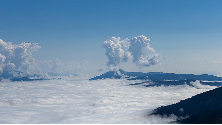 Geschlossene Wolkendecke zwischen Bergen hängend. Vereinzelt sind Wolken über der Wolkendecke und Bergen.