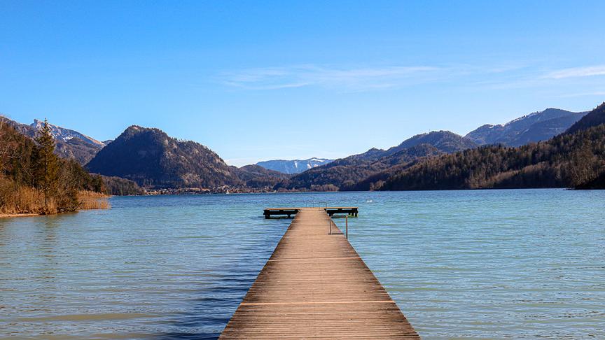 Steg führt in einen See, blauer Himmel und sonnige Stimmung, Berge im Hintergrund