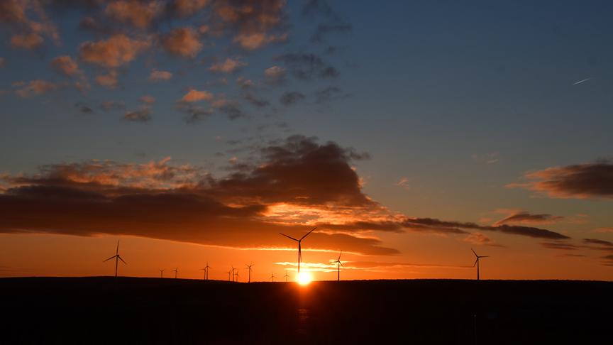 Orange-rötlicher Sonnenuntergang mit Wolken am Himmeln und Silhouetten von Windrädern im Vordergrund