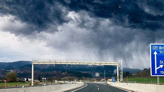 Über der Straße sind dunkle Wolken, die in Schlieren Richtung Boden ziehen.