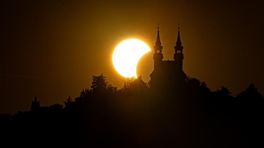 Partielle Sonnenfinsternis hinter einem Hügel mit einer Kirche.