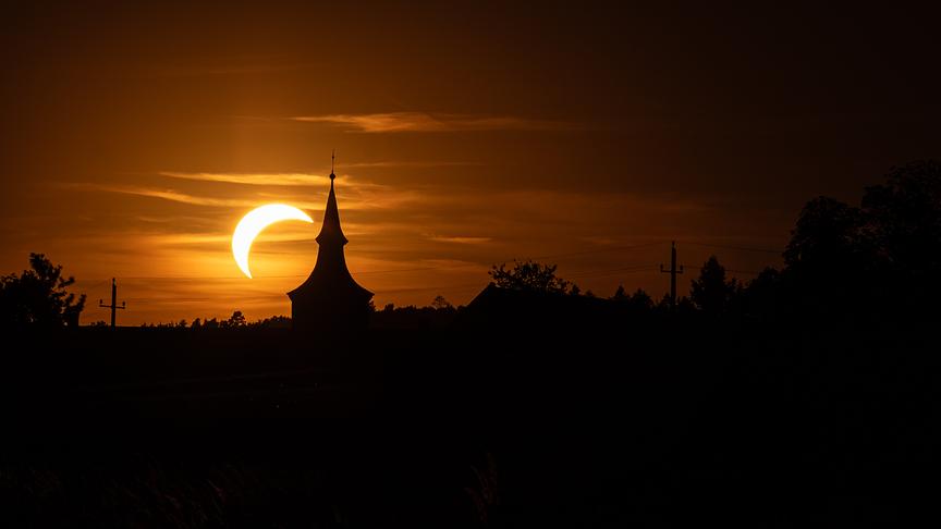 Partielle Sonnenfinsternis in warm-orangem Licht hinter der Silhouette einer Kirche.