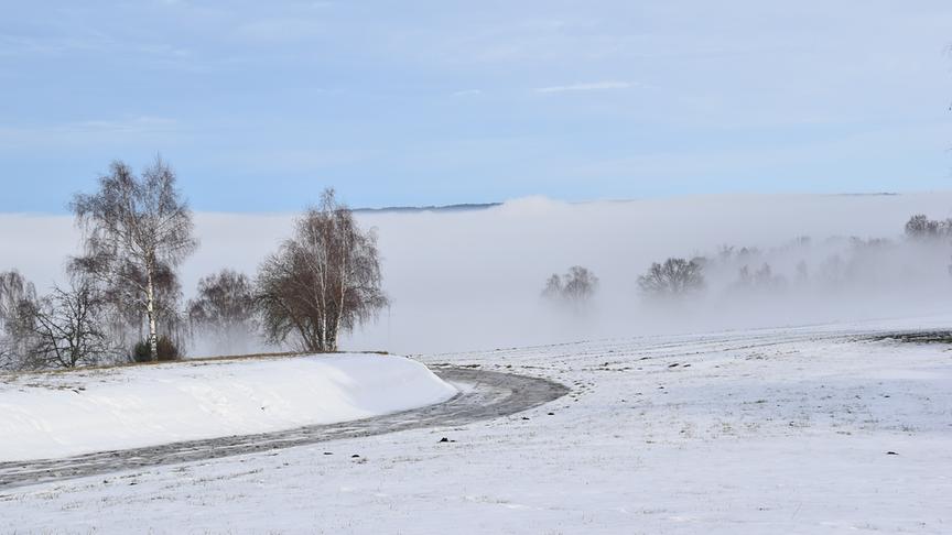 Die Straße schlängelt sich zwischen der verschneiten Landschaft hinein in den undurchsichtigen, weißen Nebel.