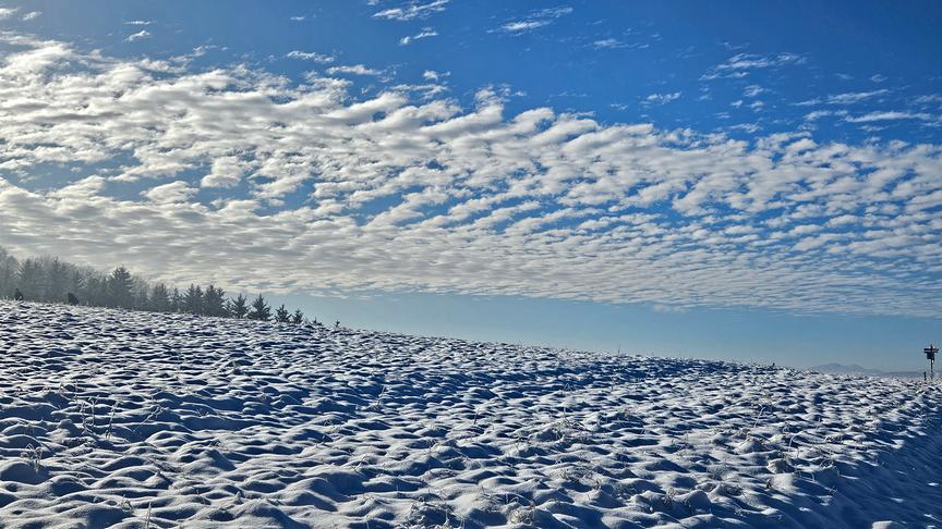Der verschneite Acker mit vielen kleinen Hügeln hat eine gewisse Ähnlichkeit mit der am blauen Himmel welligen Wolkenformation.