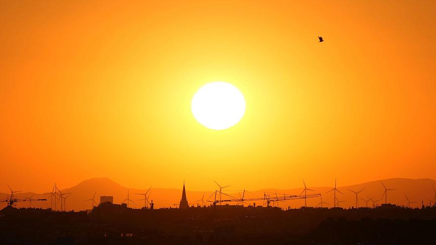Orange-warmer Sonnenuntergang über der Silhouette einer Stadt mit Windrädern und Hügeln.