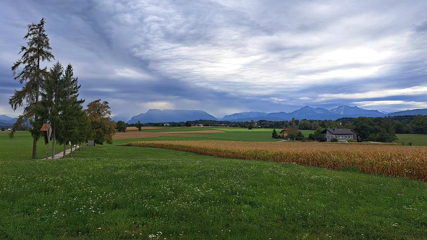 Regenstimmung über weiter Landschaft mit Feldern und Bergen.