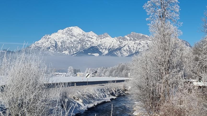 Schneepanorama mit Bach, Bergen und einem Nebelschleier