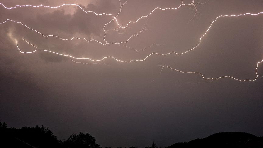 © Günther Mallweger Blitze ziehen sich horizontal über den Himmel und erhellen die Dunkelheit. Am Boden sind die Silhouetten von Bäumen zu sehen.
