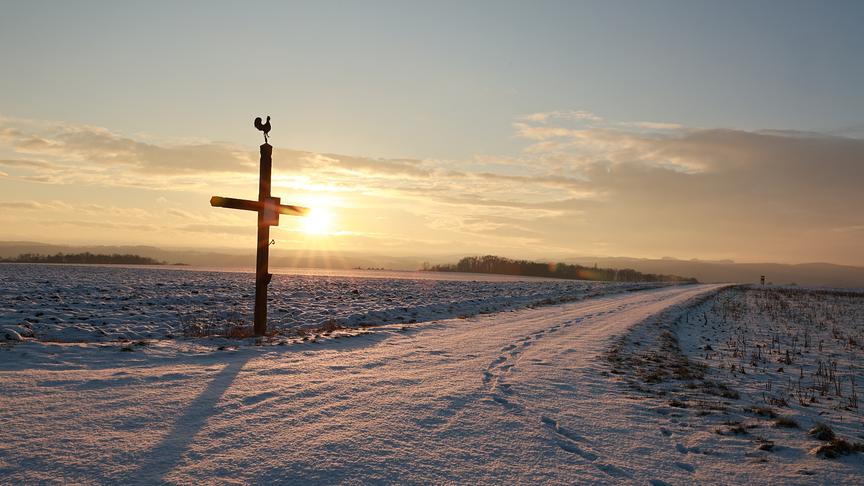 Schneebedeckter Feldweg und Felder, die Sonne scheint warm