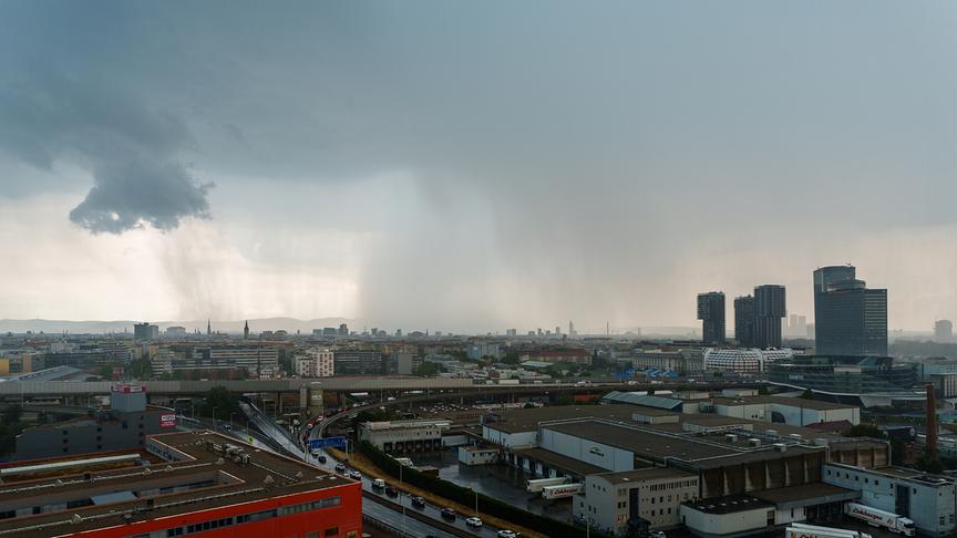 © Anita Pravits Dunkle Wolken ziehen sich in Schleiern bis zum Boden über Wien und dessen Skyline mit einigen hohen Gebäuden.