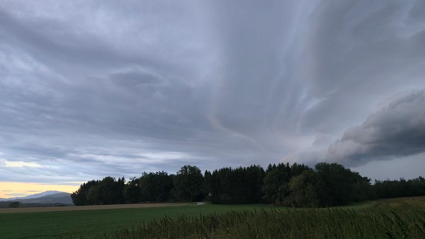 Dunkle Wolkendecke über Feldern und Wäldern.