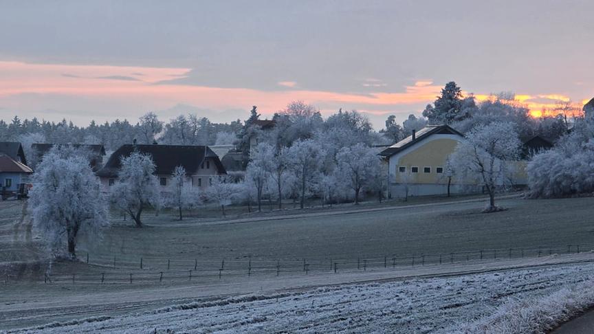 Vereiste Landschaft mit Feldern, Bäumen, Häusern und abendrotem Himmel.