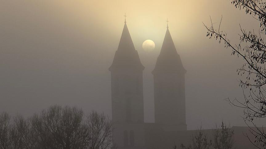 Die Sonne ist durch dichten Nebel zwischen zwei Kirchtürmen zu sehen.