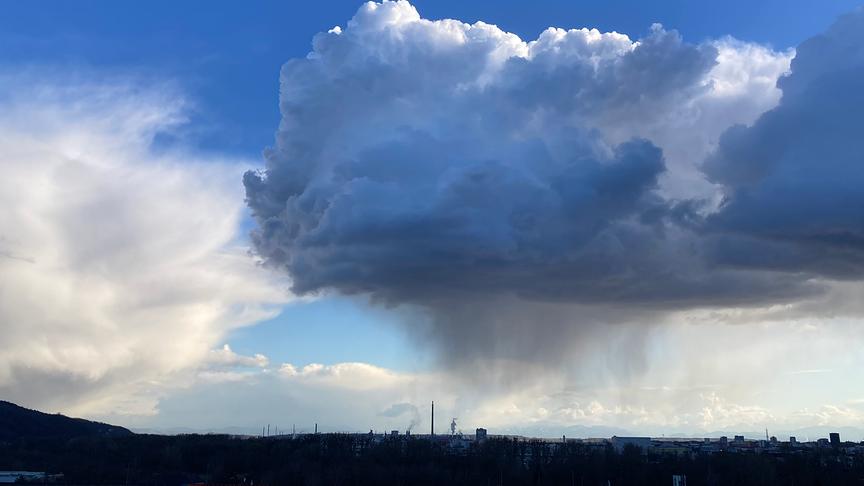 Große, hohe Wolken türmen sich über einer Stadt und ziehen Schlieren Richtung Boden
