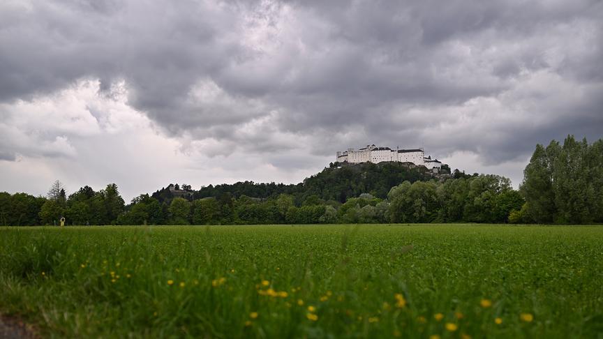 Die Festung Hohensalzburg thront auf einem bewaldeten Hügel unter dunklen Regenwolken.