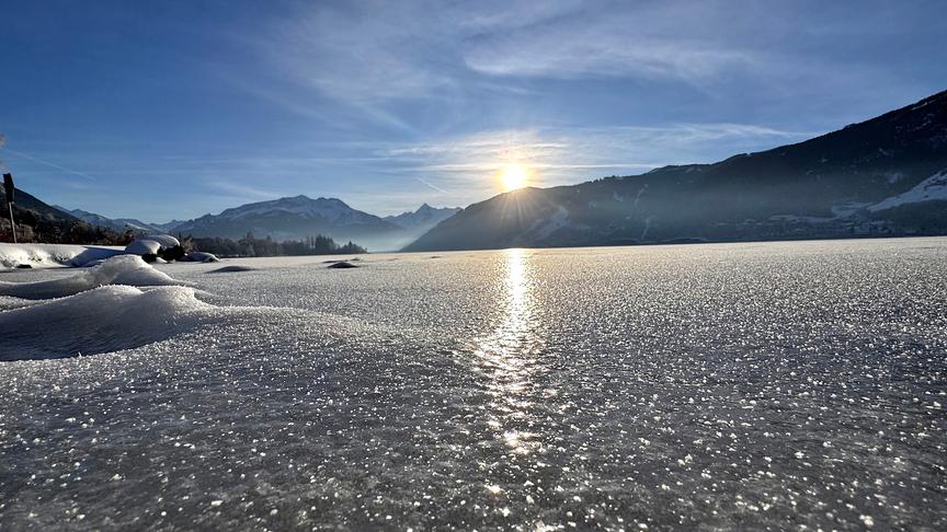 Gefrorener See mit unruhiger Oberfläche und Bergen im Hintergrund