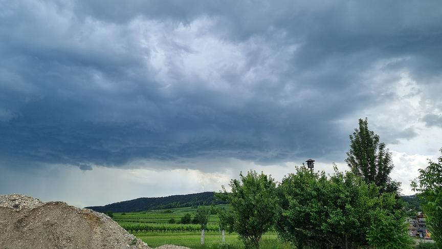 Dunkle Wolken ziehen über eine grüne Landschaft und bewegen sich in Schleiern zu Boden.