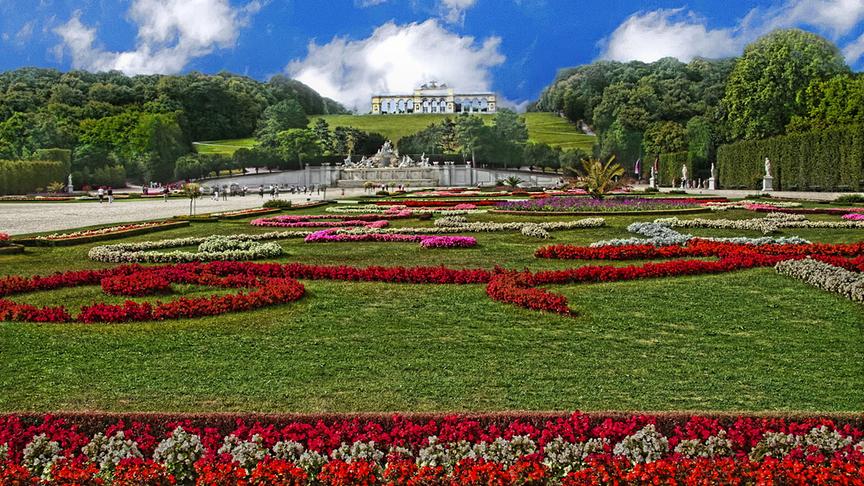 Der Schlossgarten von Schönbrunn mit kunstvollen Blumenanordnungen bei schönem Wetter. Im Hintergrund auf einem Hügel ist die Gloriette.