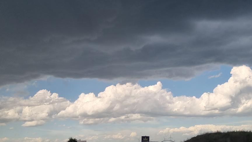 Eine dunkle Wolkendecke bedeckt den Vordergrund, während dahinter blauer HImmel mit bauschigen Wolken einen Kontrast bilden.